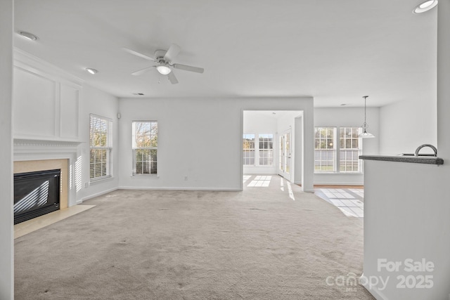 unfurnished living room featuring light colored carpet, a high end fireplace, ceiling fan, and baseboards
