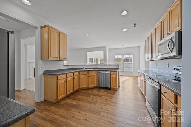kitchen with a peninsula, dark countertops, recessed lighting, appliances with stainless steel finishes, and a sink