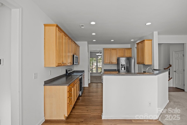 kitchen with recessed lighting, dark countertops, a peninsula, appliances with stainless steel finishes, and wood finished floors