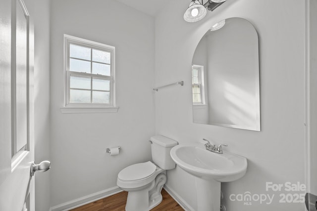 half bath with baseboards, toilet, and wood finished floors
