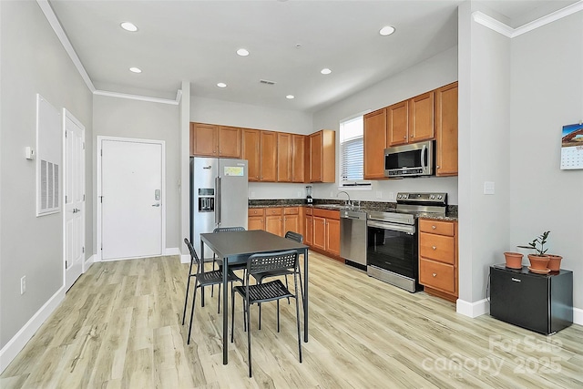 kitchen featuring appliances with stainless steel finishes, light wood-type flooring, baseboards, dark countertops, and ornamental molding