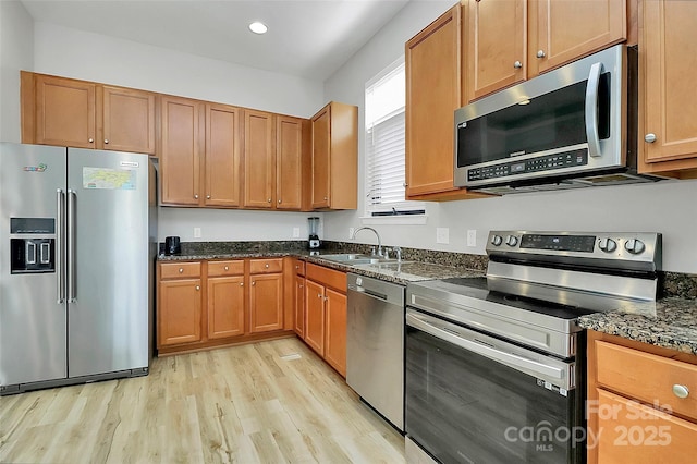 kitchen with dark stone counters, a sink, stainless steel appliances, and light wood finished floors