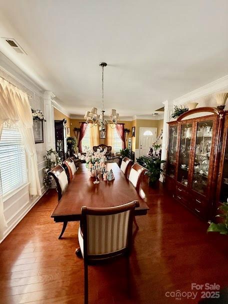 dining room with wood finished floors, visible vents, a chandelier, and ornamental molding