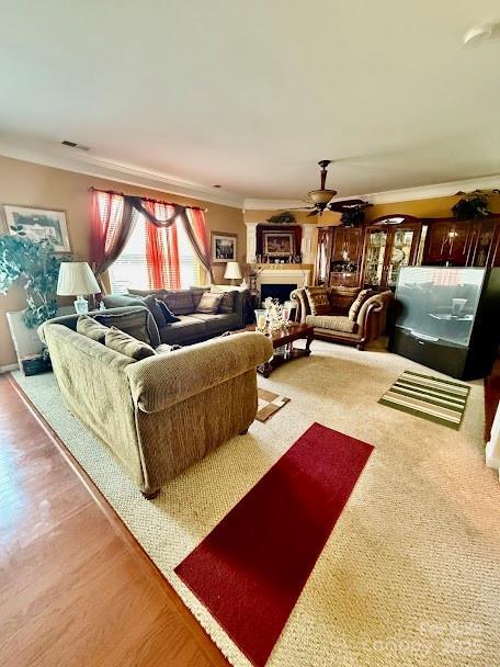 living area with a fireplace, crown molding, visible vents, and a ceiling fan