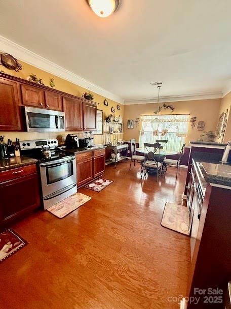 kitchen with dark wood finished floors, dark countertops, crown molding, hanging light fixtures, and appliances with stainless steel finishes