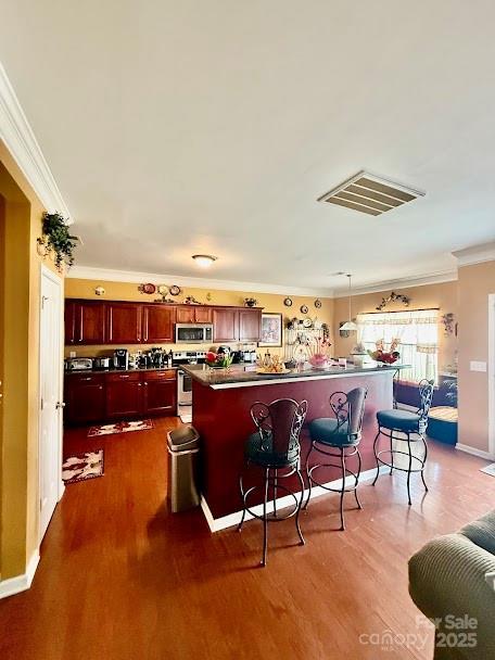 kitchen featuring stainless steel appliances, dark brown cabinets, visible vents, a breakfast bar, and ornamental molding