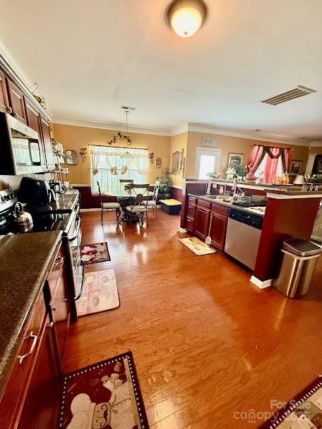 kitchen with stainless steel appliances, pendant lighting, ornamental molding, dark wood-type flooring, and visible vents