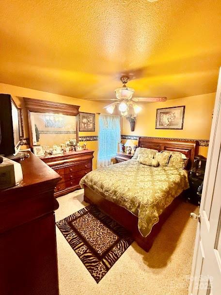 carpeted bedroom featuring a ceiling fan and a textured ceiling