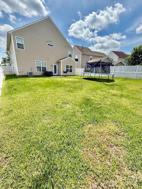 rear view of property featuring a trampoline, a lawn, and a fenced backyard