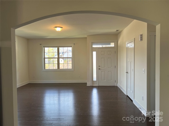 entryway featuring baseboards, arched walkways, and dark wood-style flooring