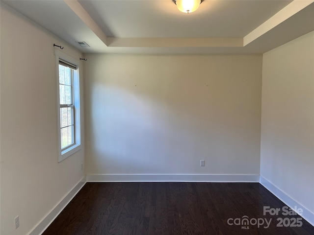 empty room featuring baseboards, dark wood-style floors, visible vents, and a raised ceiling