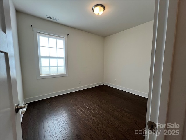 empty room featuring dark wood finished floors, baseboards, and visible vents