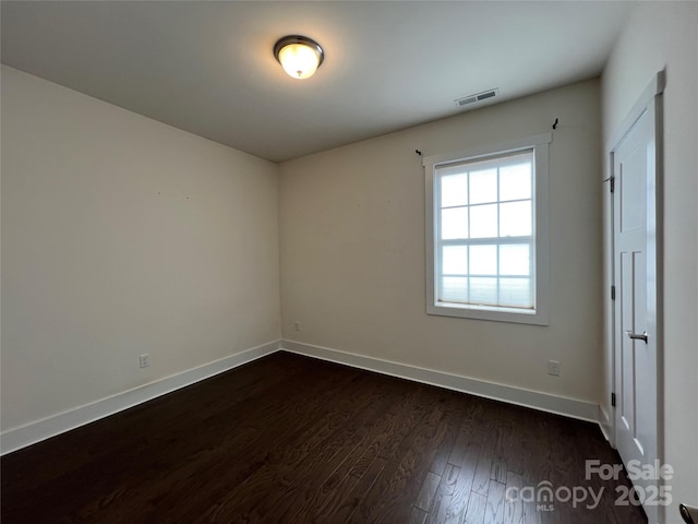 spare room with baseboards, visible vents, and dark wood finished floors