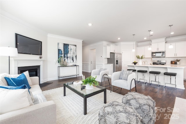 living area with a glass covered fireplace, recessed lighting, dark wood-style flooring, and ornamental molding