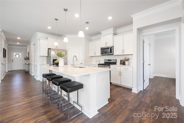 kitchen with a kitchen breakfast bar, ornamental molding, a kitchen island with sink, stainless steel appliances, and a sink