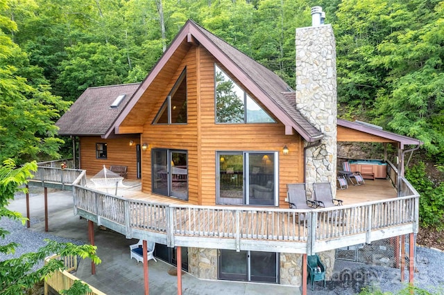 rear view of property featuring a forest view, a chimney, a wooden deck, a jacuzzi, and stone siding