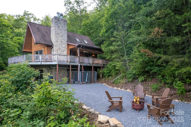 rear view of property with stone siding, a deck, a patio, a chimney, and an outdoor fire pit
