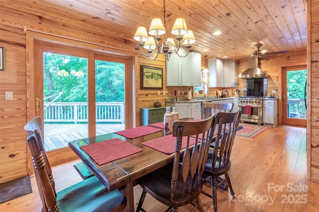 dining room with wood walls, wood ceiling, ceiling fan with notable chandelier, and light wood-type flooring