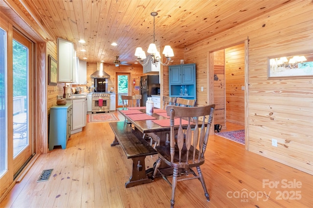 dining area with wooden walls, a notable chandelier, plenty of natural light, light wood-style flooring, and visible vents