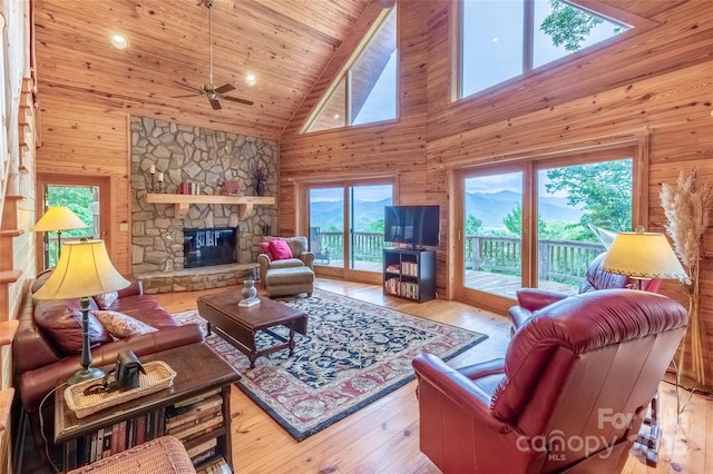 living area featuring high vaulted ceiling, ceiling fan, wood walls, and a stone fireplace