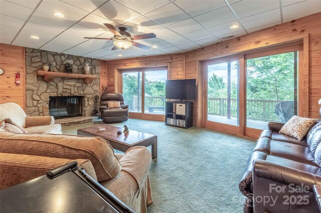 carpeted living room with a ceiling fan, a paneled ceiling, visible vents, a fireplace, and wooden walls