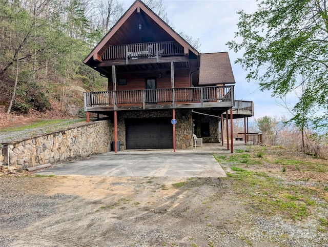 chalet / cabin featuring a garage, a balcony, a deck, stone siding, and concrete driveway