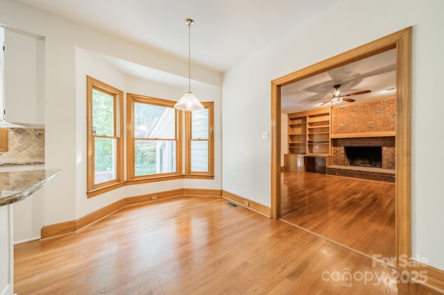 5232 Silchester Ln, Charlotte, NC 28215 - unfurnished dining area featuring light wood finished floors, baseboards, built in shelves, a brick fireplace, and ceiling fan