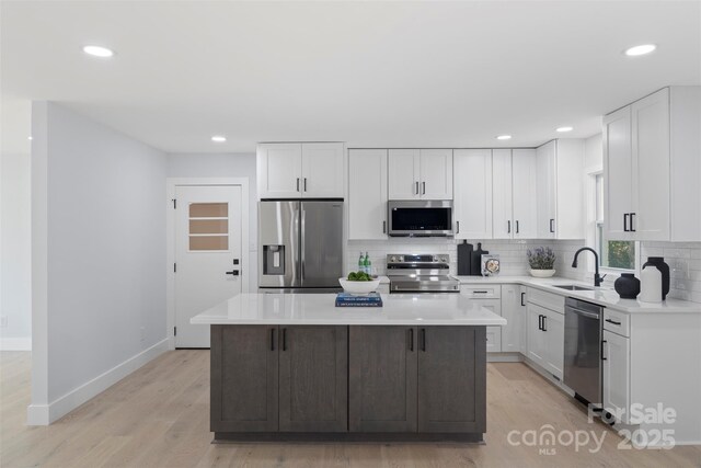 1315 Vickie Ln, Matthews, NC 28104 - kitchen with stainless steel appliances, light wood-style floors, backsplash, a kitchen island, and white cabinetry