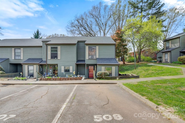 multi unit property featuring roof with shingles, a front lawn, and uncovered parking
