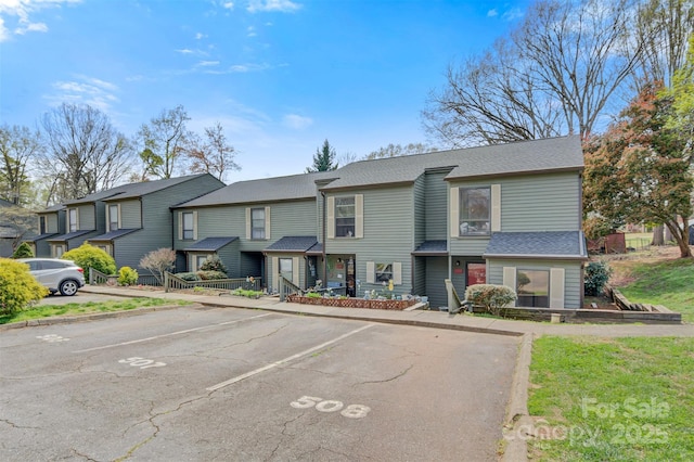 multi unit property with uncovered parking, roof with shingles, and a residential view