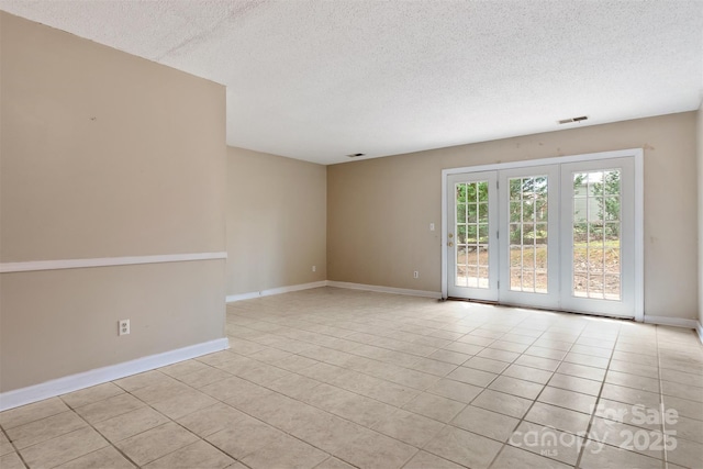 empty room with a textured ceiling, light tile patterned flooring, baseboards, and visible vents