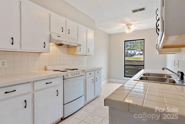 kitchen with under cabinet range hood, tile countertops, a sink, and electric range