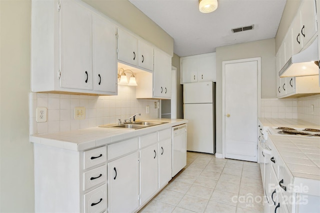 kitchen featuring a sink, white appliances, tile countertops, visible vents, and backsplash