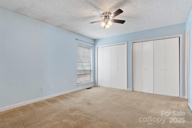 unfurnished bedroom with a textured ceiling, visible vents, two closets, ceiling fan, and carpet floors
