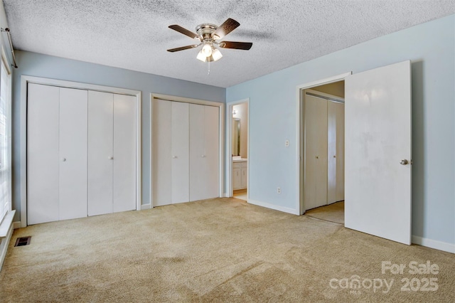 unfurnished bedroom featuring two closets, a textured ceiling, and carpet