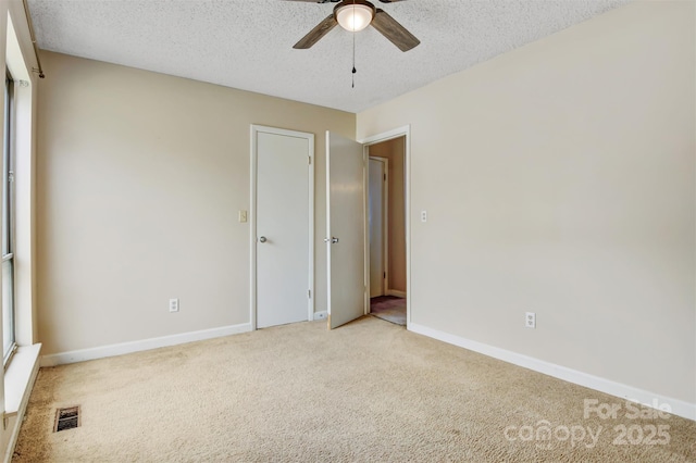empty room featuring light colored carpet, a textured ceiling, visible vents, and ceiling fan