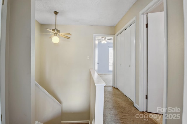 hallway featuring a textured ceiling, carpet flooring, and an upstairs landing