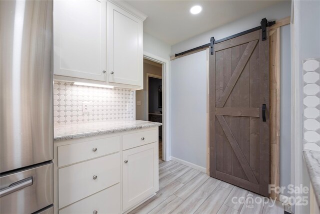 4487 Catawba Burris Rd, Denver, NC 28037 - kitchen featuring light stone counters, freestanding refrigerator, white cabinetry, a barn door, and decorative backsplash