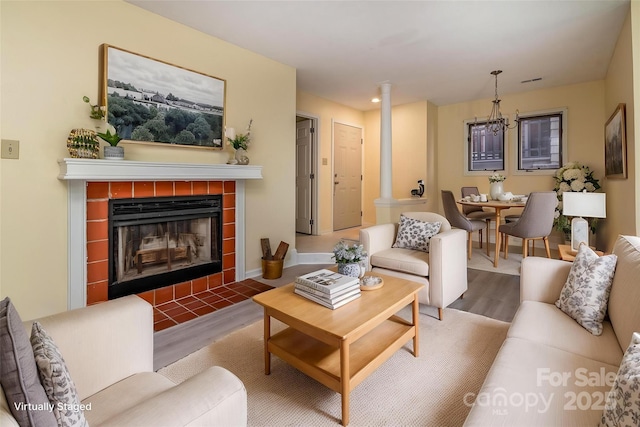 living area with a tiled fireplace, a chandelier, ornate columns, and wood finished floors