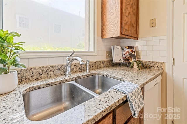 kitchen featuring white dishwasher, light stone counters, decorative backsplash, and a sink