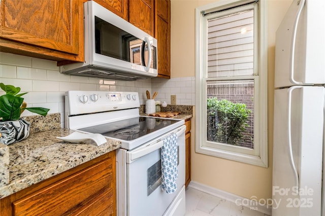 kitchen with decorative backsplash, white appliances, baseboards, and brown cabinets