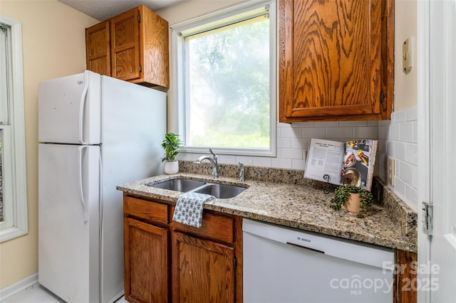 kitchen featuring brown cabinetry, white appliances, light stone counters, a sink, and backsplash