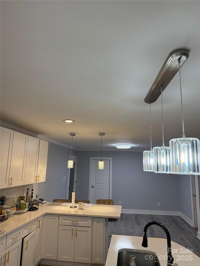 kitchen with a peninsula, wood finished floors, baseboards, a sink, and hanging light fixtures