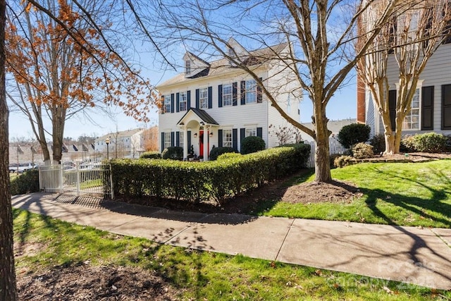 colonial inspired home with a gate, fence, and a front lawn