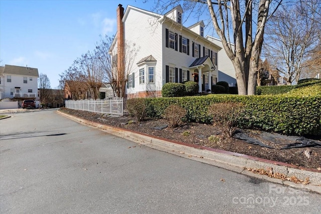 view of side of property with a chimney, fence, and aphalt driveway