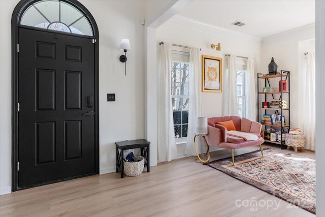 entrance foyer featuring visible vents, light wood-style flooring, and crown molding