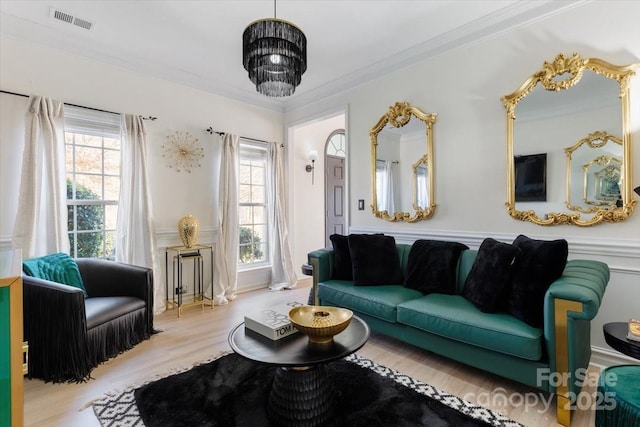 living room featuring wood finished floors, a wealth of natural light, crown molding, and visible vents