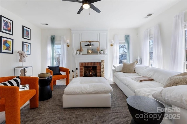 living room featuring a wealth of natural light, visible vents, a ceiling fan, and a brick fireplace