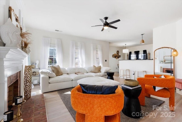 living area featuring a fireplace, ceiling fan, visible vents, and wood finished floors