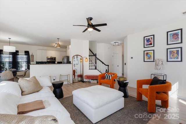 living room featuring light wood finished floors, visible vents, ceiling fan, and stairway